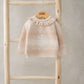 Light beige snowflake knit jumper with ruffled high neck hanging on wooden display