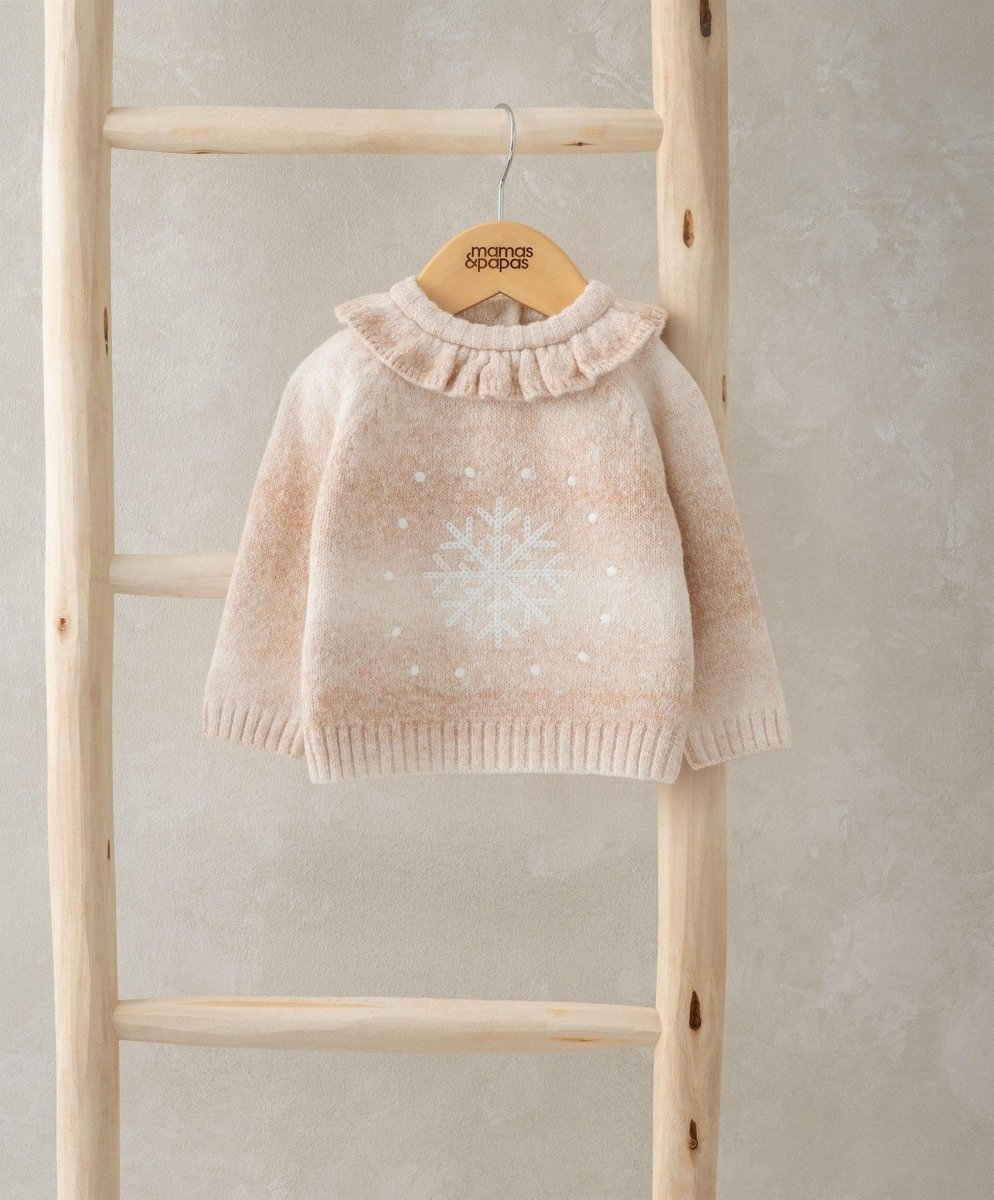 Light beige snowflake knit jumper with ruffled high neck hanging on wooden display