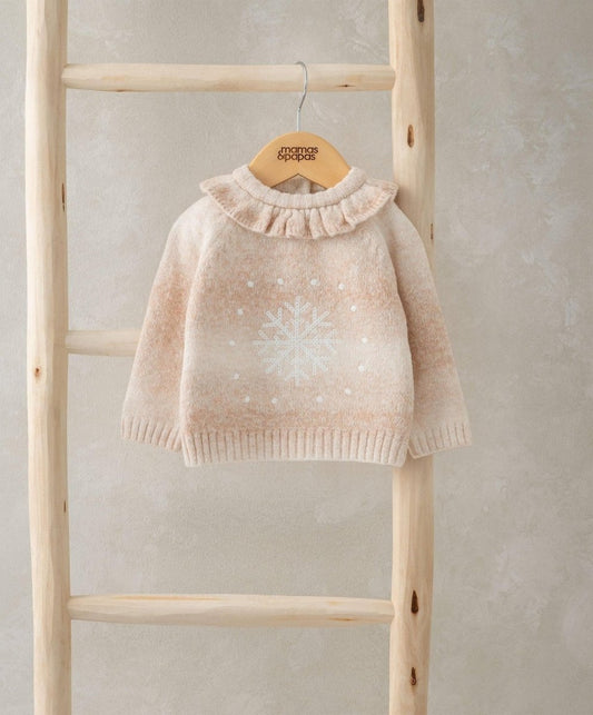 Light beige snowflake knit jumper with ruffled high neck hanging on wooden display