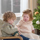 Light beige snowflake knit jumper with ruffled high neck on seated child indoors
