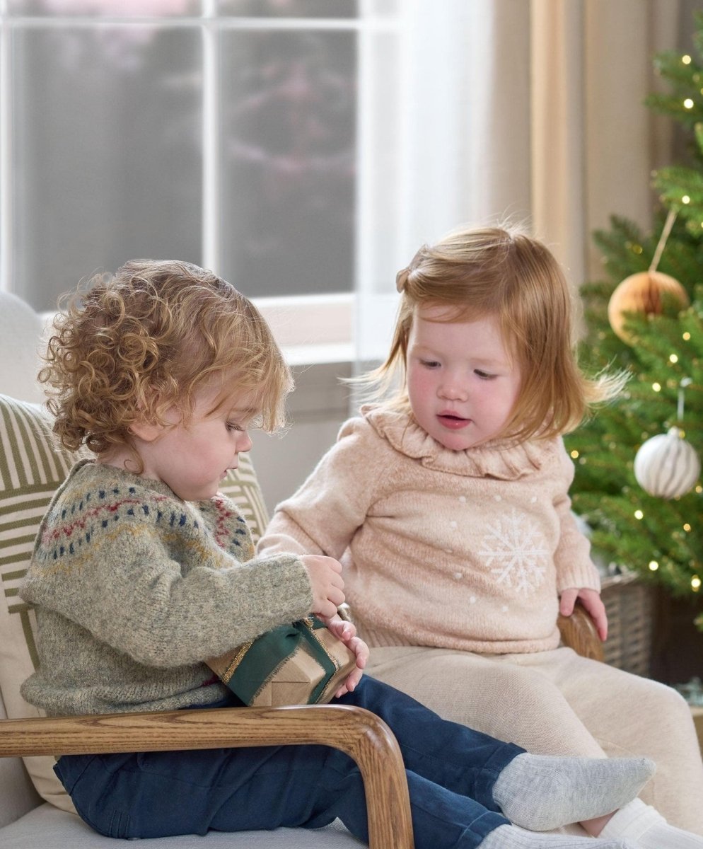 Light beige snowflake knit jumper with ruffled high neck on seated child indoors