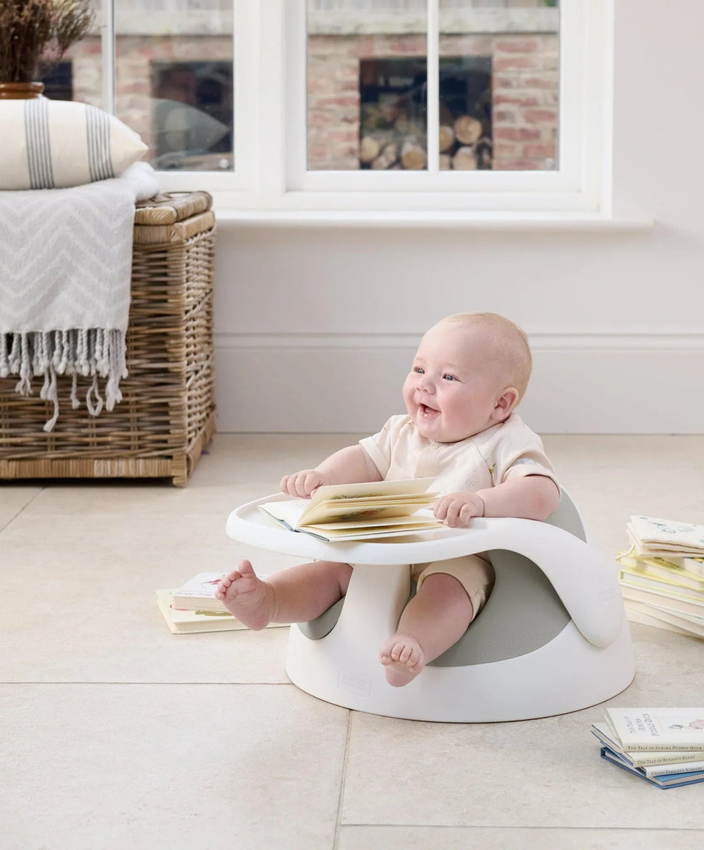 Baby floor seat with activity tray, white base, baby reading book on seat