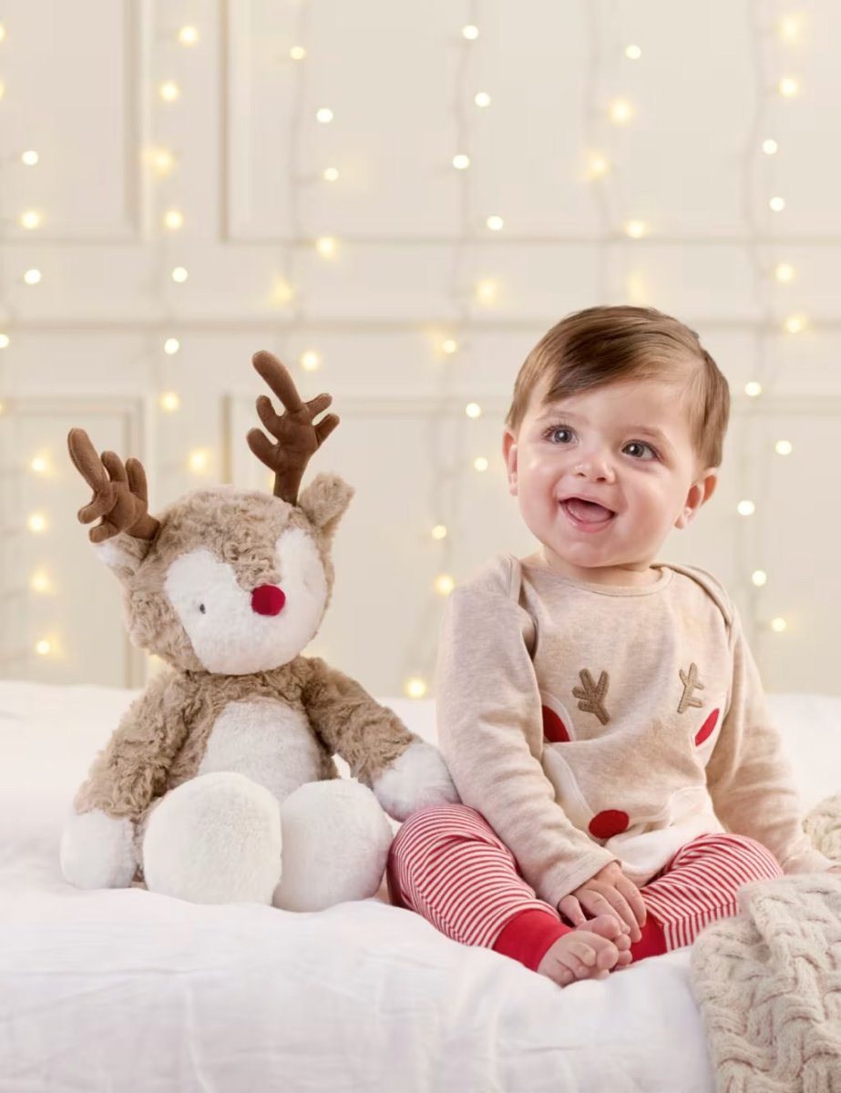 Plush reindeer soft toy with red nose and brown antlers beside a baby on a bed