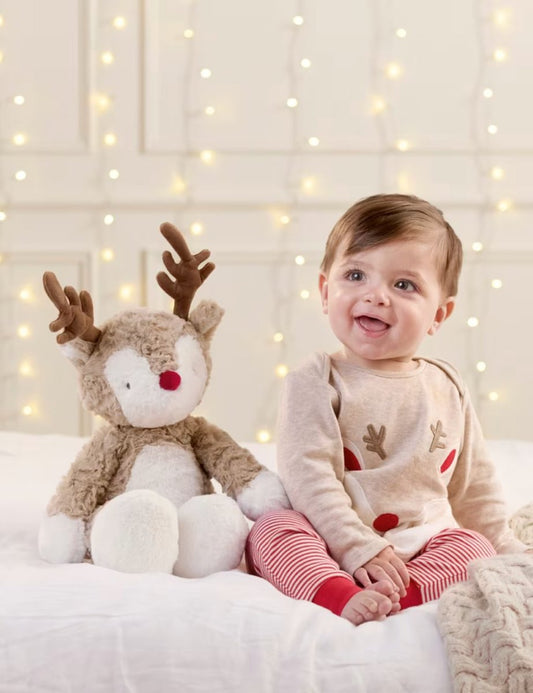 Plush reindeer soft toy with red nose and brown antlers beside a baby on a bed
