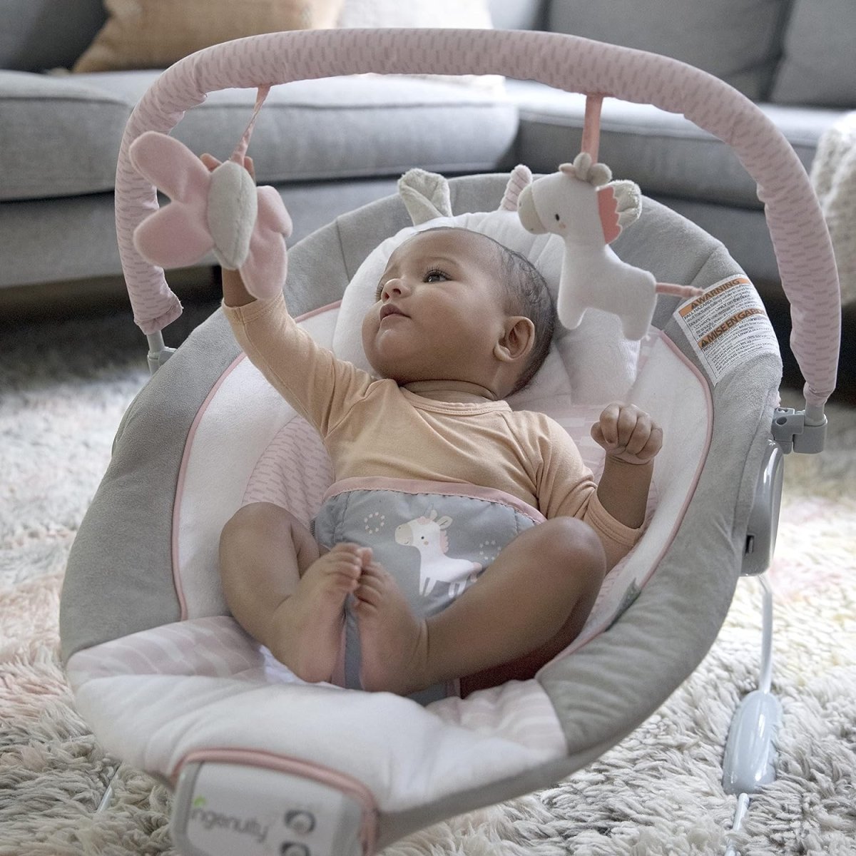 Infant reclining in gray and pink bouncer on a soft rug