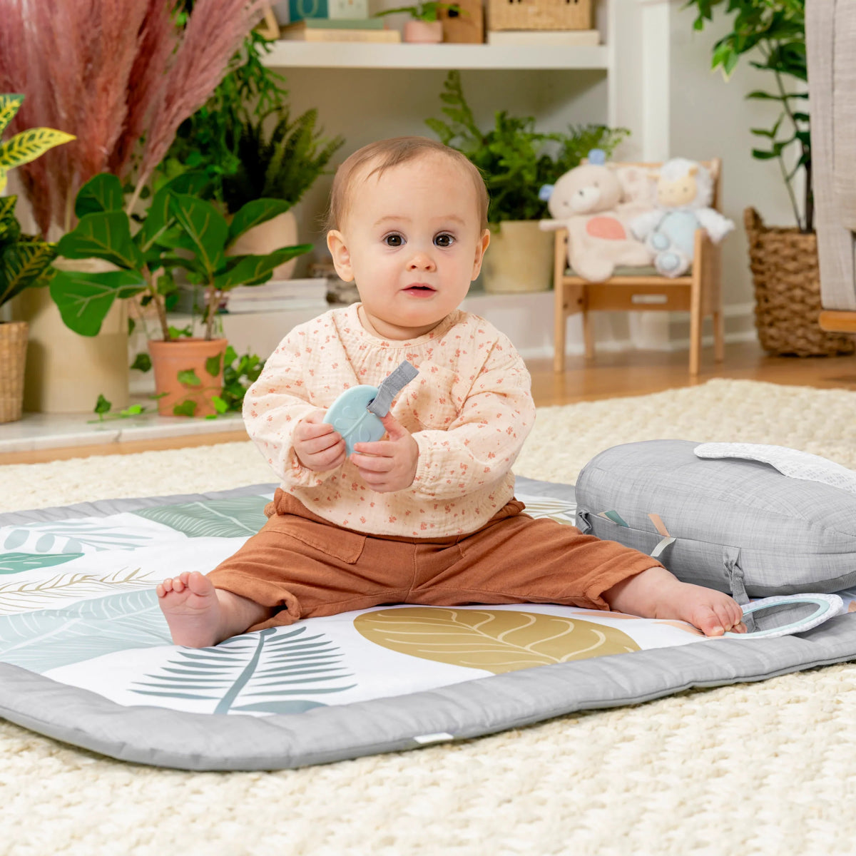Baby on tummy time play mat with jungle leaf print and gray elephant pillow toy