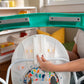 Front view of white activity walker seat with colorful fabric and open base