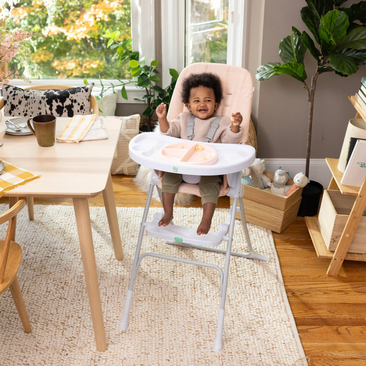 Blush high chair with white tray and seated toddler, side view.