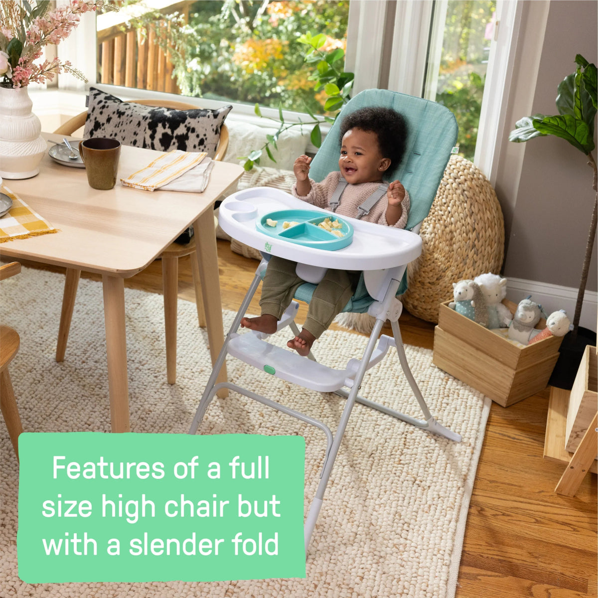 Teal high chair with white tray and seated toddler, side view.