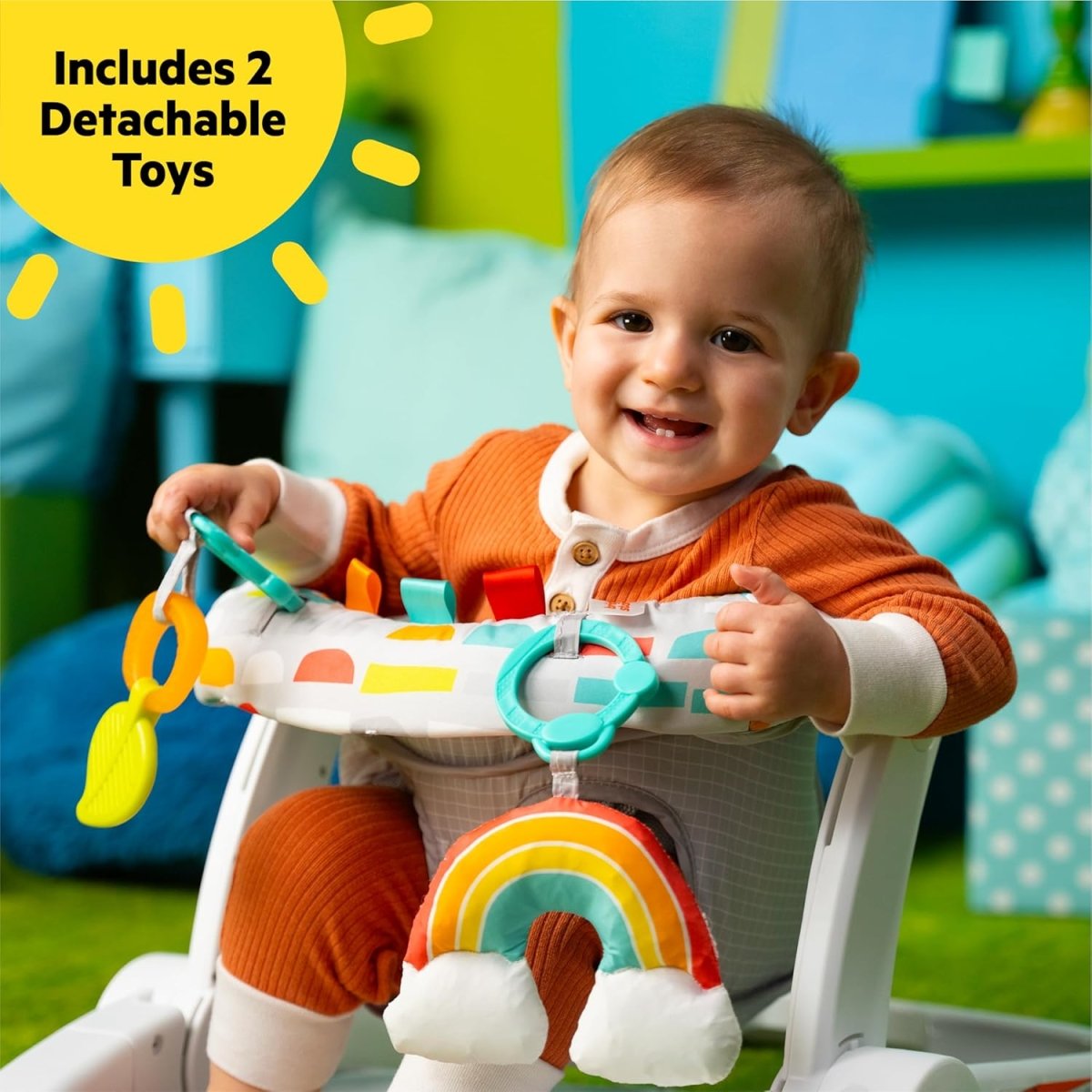 Baby seated in a white play chair with gray pad and rainbow hanging toy bar