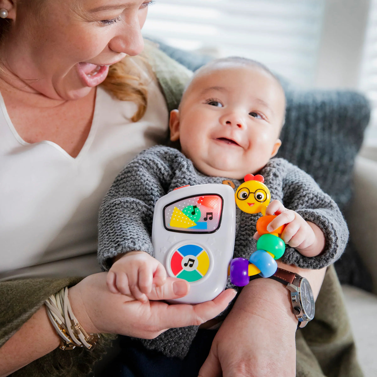 Handheld musical toy with bright icon panel and character figure, held by baby