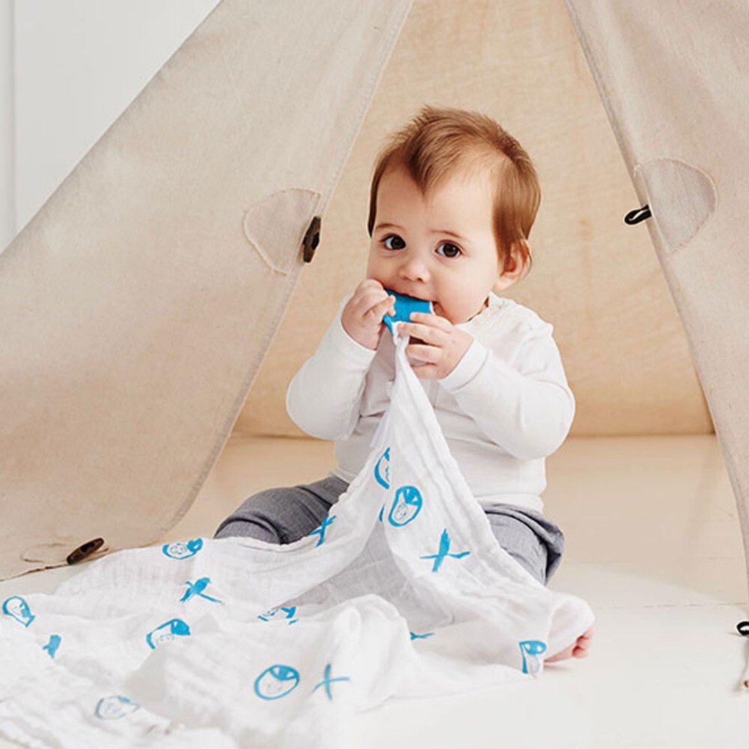 Muslin baby blanket with blue motifs while baby sits in a play tent