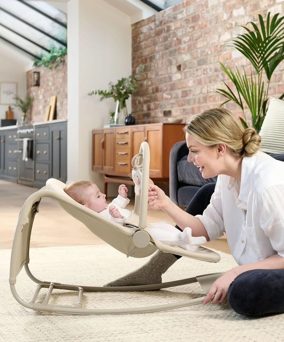 Baby rocker and bouncer with magnetic toy bar, light tan seat, baby reclined