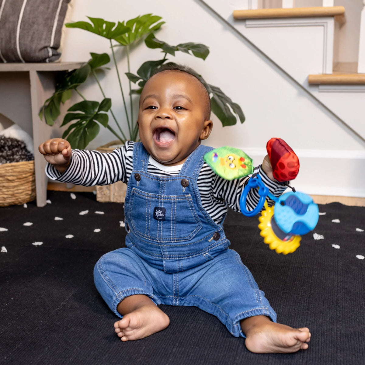 Baby holding a hanging sensory toy with fabric animal shapes and bright sun
