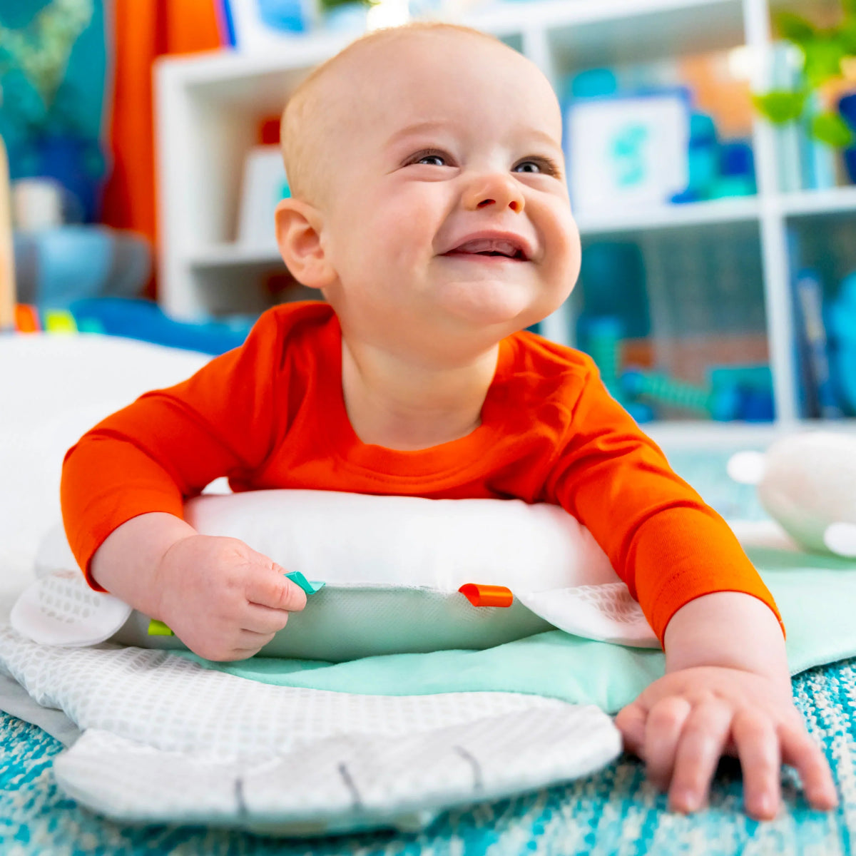 Baby smiling in orange shirt on teal and white activity mat with crinkle edges