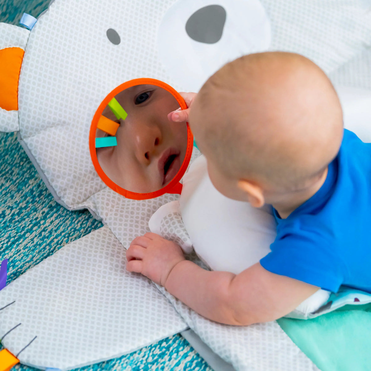 Baby on white activity mat with polar bear hood and orange ring teether
