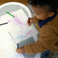Baby kneeling at a play center, drawing on a colorful scribble activity board