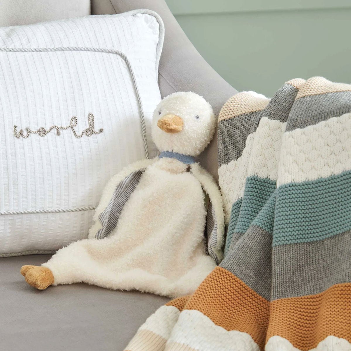 Plush duck comforter lying on sofa beside striped pillows