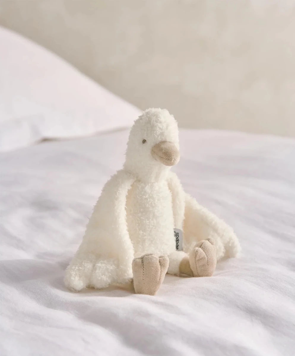 Cream duckling plush toy sitting on bed, with small wings and plush feet