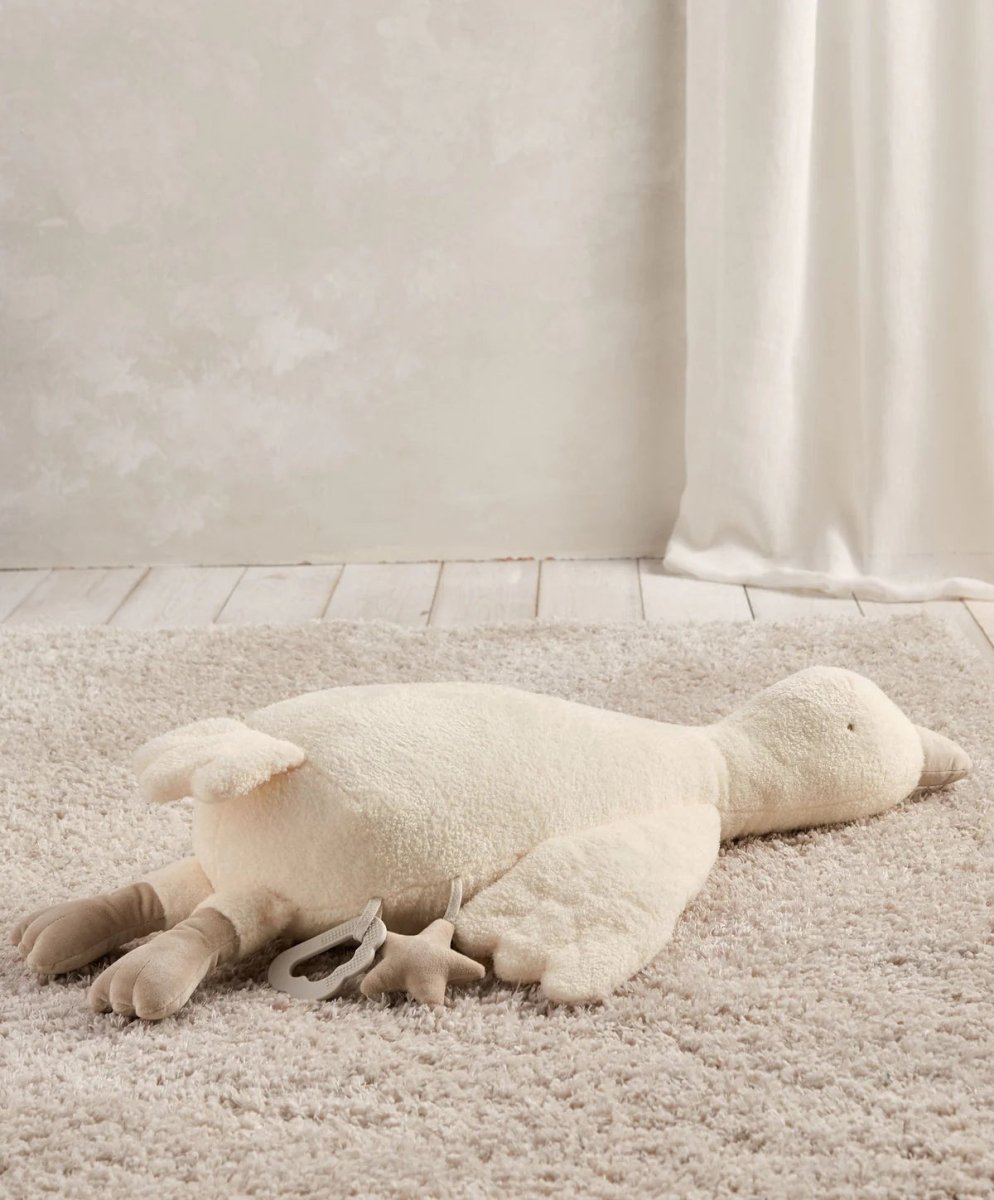 Plush tummy time duck in light cream, belly-down with arms and wings extended.