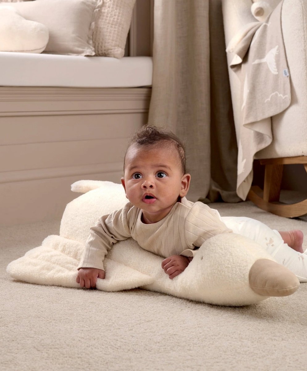 Baby on a light cream plush tummy time duck, belly-down on the padded support.