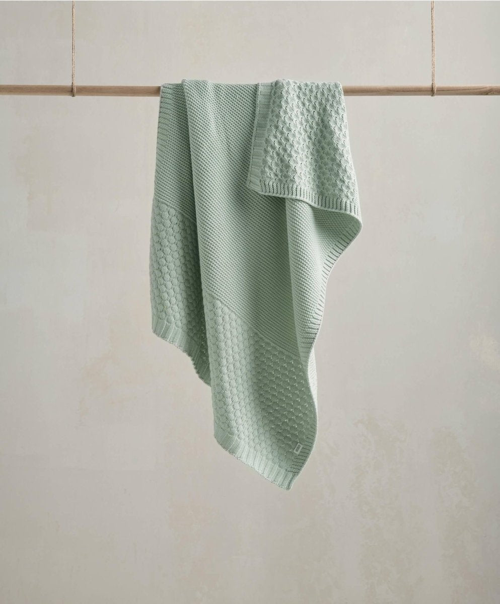 Knitted blanket in mint green with textured waffle pattern, draped over a display