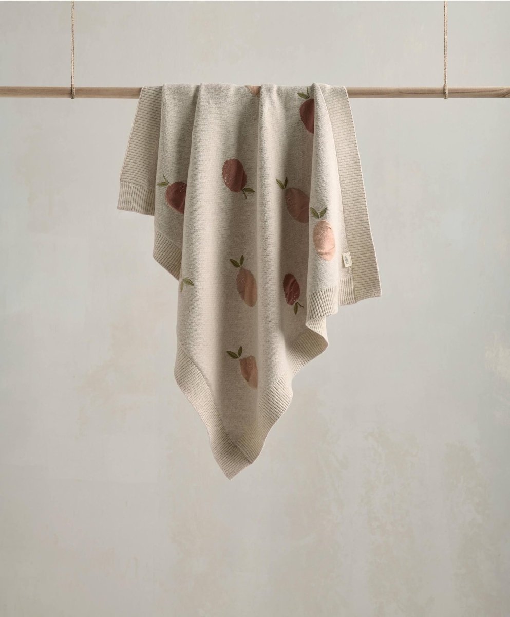 Knitted baby blanket with fruit print, light beige with peach and leaf motifs