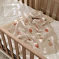 Knitted baby blanket draped over wooden crib rail, light beige with fruit and leaf pattern