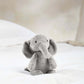 Small plush elephant toy, light gray sitting with trunk curled under chin