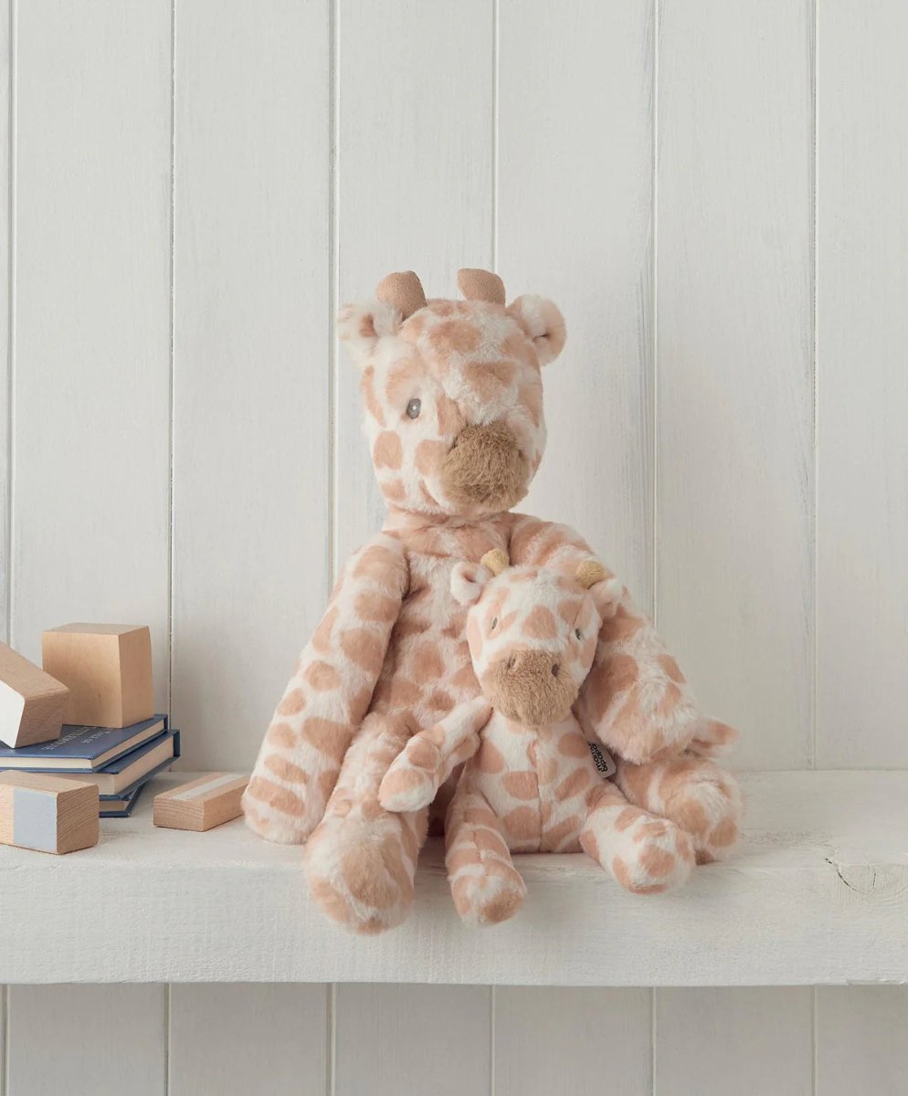 Small plush giraffe toy sitting on a shelf, beige fur with brown spots