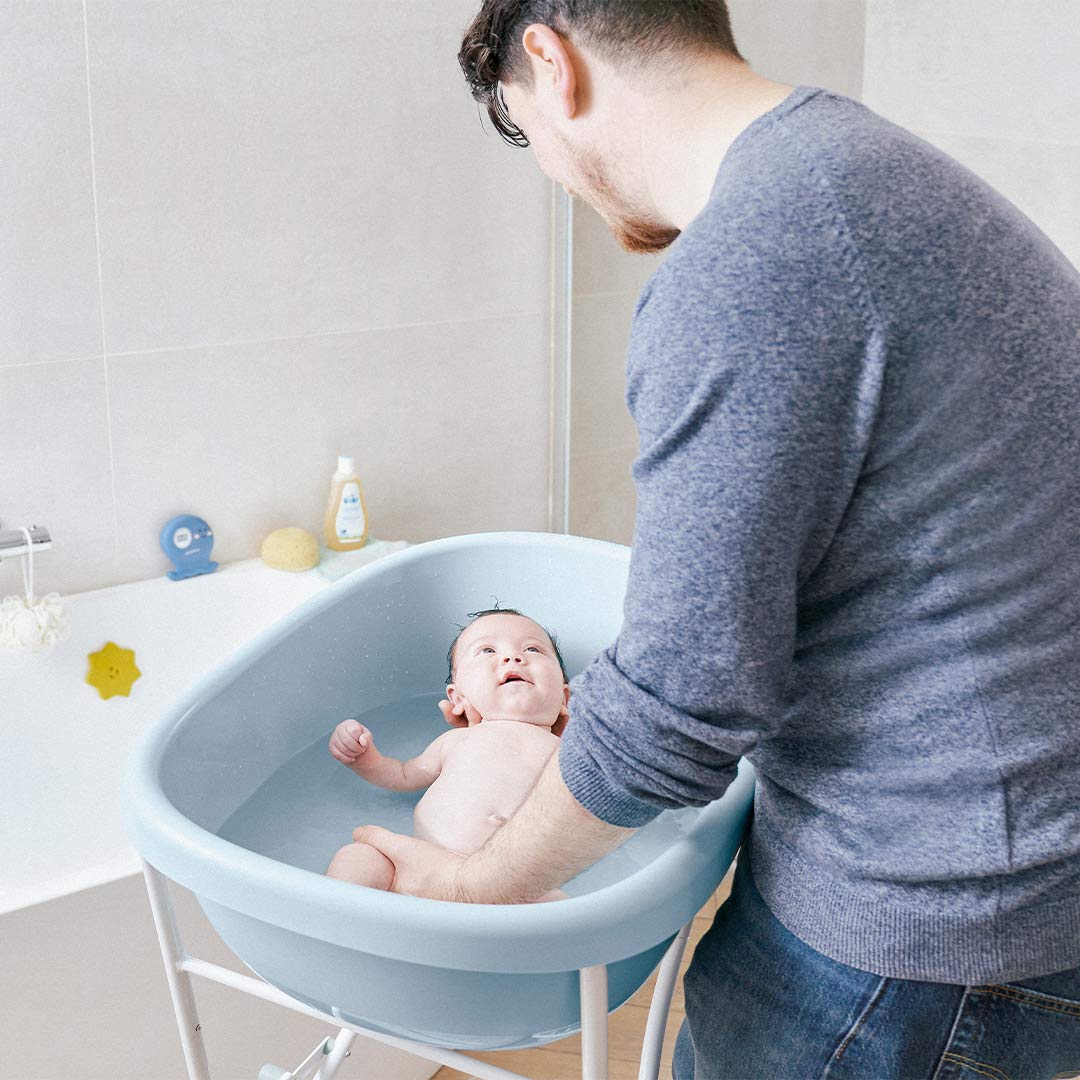 Baby bath tub on stand, light blue oval basin with infant inside