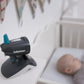 Baby monitor camera on a crib edge, black and gray body with teal antenna