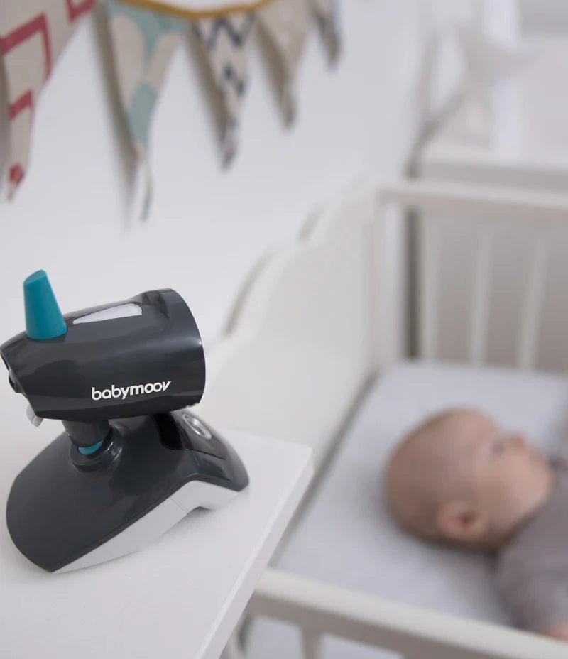 Baby monitor camera on a crib edge, black and gray body with teal antenna