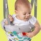Door jumper seat with baby wearing white top, gray striped safety harness and patterned fabric